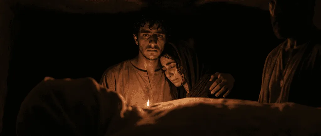 A young man holding a grieving woman by candlelight